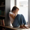 anxiété symptômes et solutions naturelles, femme assise près d’une fenêtre dans un moment de tension émotionnelle.