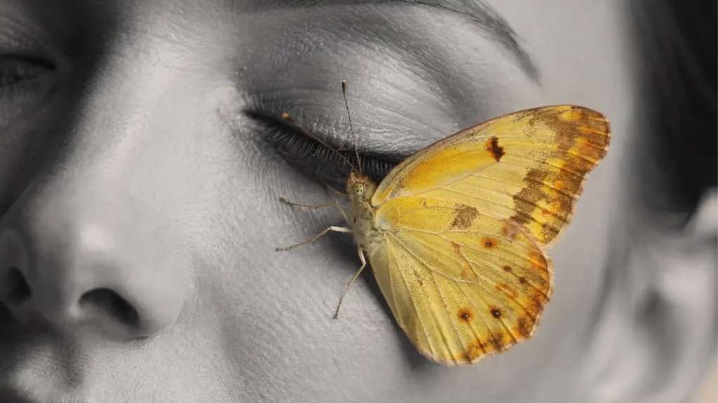 Visage apaisé avec un papillon jaune posé délicatement, illustrant la transformation et la douceur du massage métamorphique.