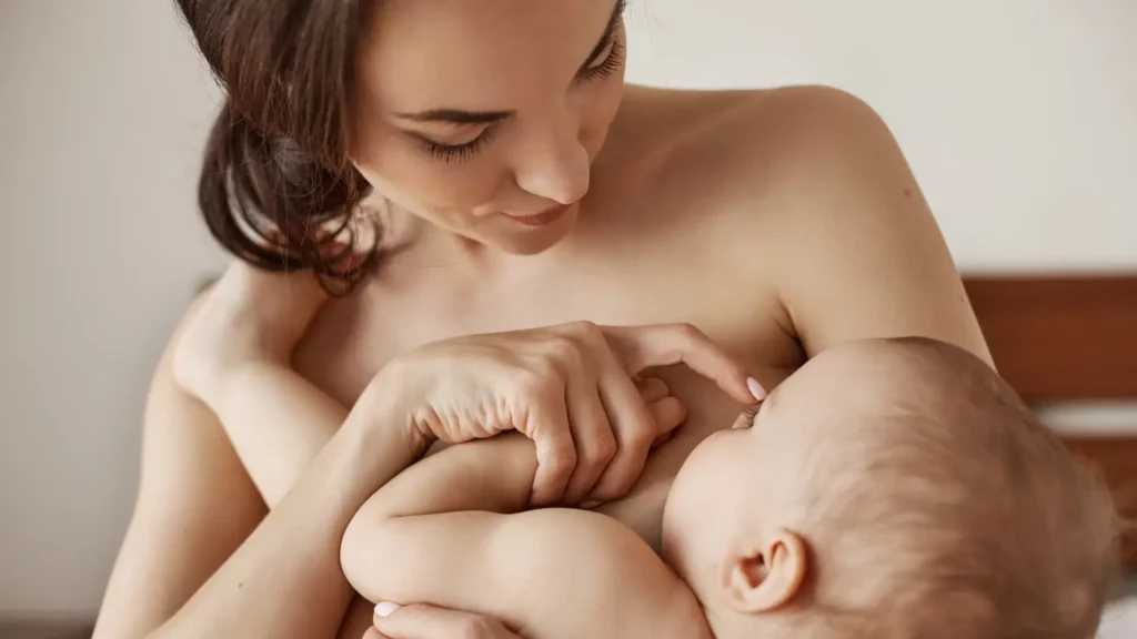 Mère souriante en contact peau à peau avec son bébé, le touchant doucement sur le nez, illustrant un moment de complicité après l'allaitement.