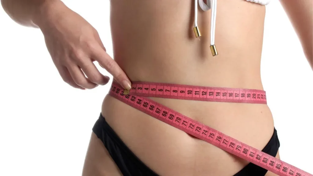 Femme mesurant son tour de taille avec un mètre ruban rose pour évaluer les effets du massage amincissant.